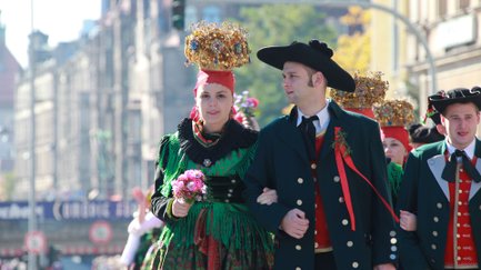 Teilnehmende in farbenfroher Tracht laufen beim Erntedankfestzug der Michaelis-Kirchweih durch die Stadt.