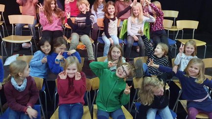 Kinder sitzen in mehreren Reihen und ziehen fröhliche Grimassen bei einer Aktion der Kirchenmusiktage.