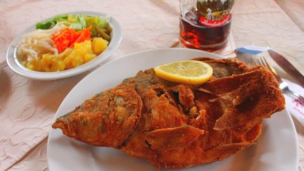Ganz gebackener, knuspriger Karpfen mit Zitronenscheibe, Beilagensalat und einem Glas Dunkelbier.