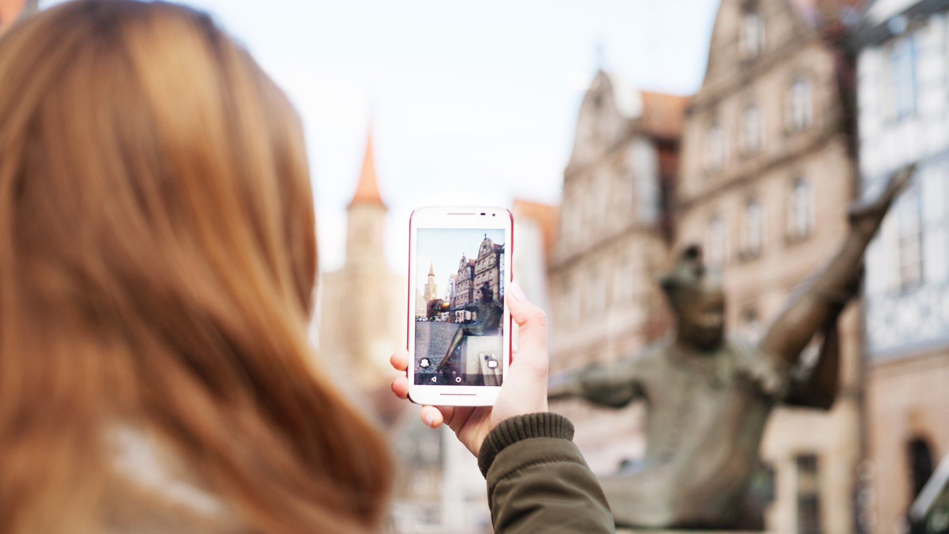Junge Touristin macht ein Foto vom Gauklerbrunnen am Grünen Markt in Fürth mit der Kirche St. Michael im Hintergrund.