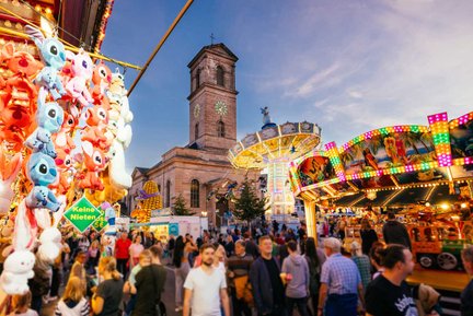Besucher:innen an der Michaelis Kirchweih vor dem leuchtenden Kettenkarussell und der Kirche Unsere Liebe Frau.