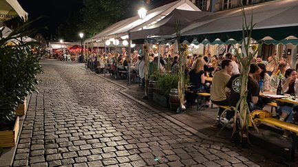Besucher sitzen vor den Lokalen der Gustavstraße und genießen beim Weinfest gemeinsam den Abend bei einem Getränk.