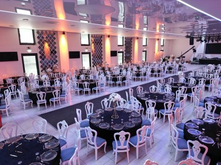 Große Halle im First Class Event Fürth mit runden Tischen, verzierten weißen Stühlen und Bühne