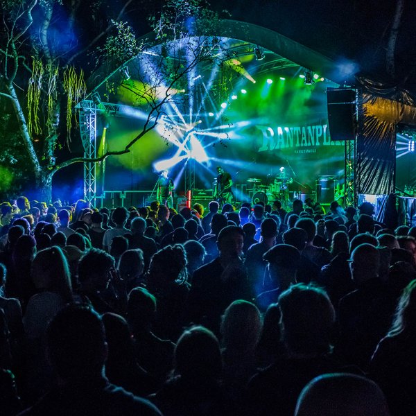 Publikum schaut auf die farbig beleuchtete Bühne des Open-Air am Lindenhain, auf der eine Band spielt