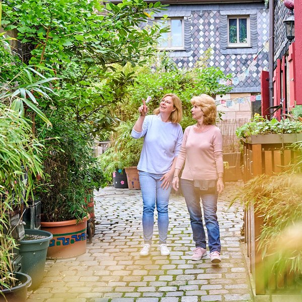 Zwei Frauen spazieren durch einen idyllischen Hinterhof in der Pfarrgasse in der Fürther Altstadt, umgeben von Sandsteinhäusern und blühenden Pflanzen.