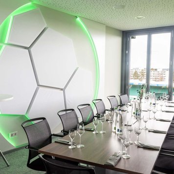 Kleiner Konferenzraum mit langem Holztisch, Stühlen, Gläsern, Wasserflaschen und Fußball-Wanddeko