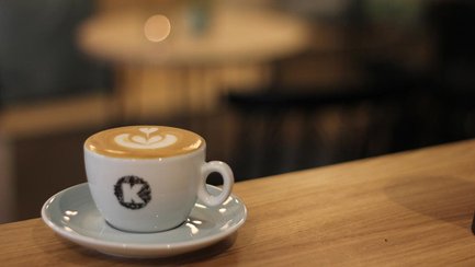 Eine weiße Tasse Cappuccino mit Latte Art auf einer Untertasse auf einem hölzernen Tresen.
