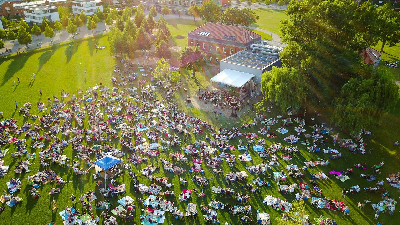 Besucher sitzen auf Picknickdecken im Südstadtpark und hören dem Orchester beim Open-Air-Konzert zu