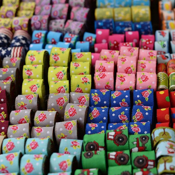 Mehrere bunte Stoffrollen mit verschiedenen Motiven liegen geordnet zur Präsentation auf dem Stoffmarkt.