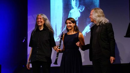 Drei Künstler halten sich nach ihrem Auftritt auf der Bühne vor der Projektion einer jungen Komponistin.