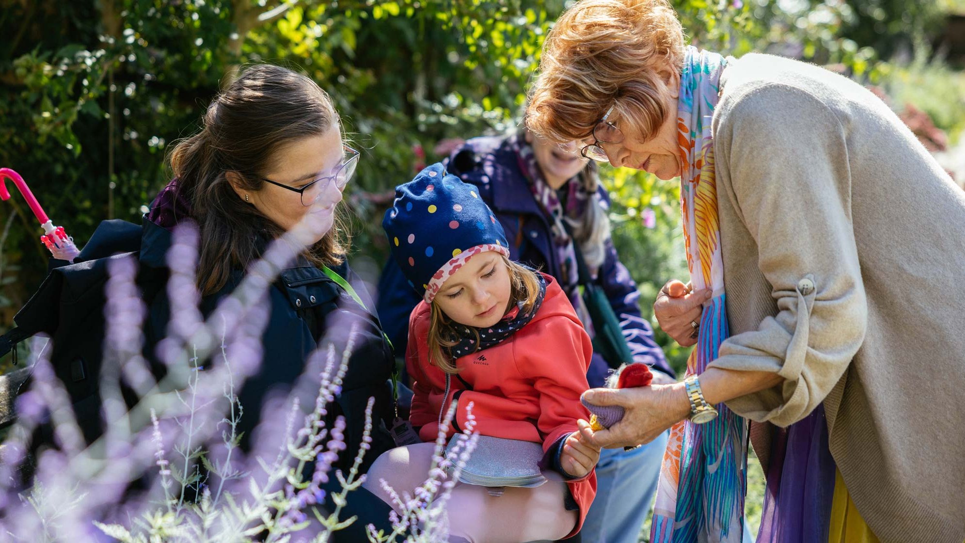 Märchenerzählerin zeigt einem Mädchen auf dem Schoß der Mutter eine Puppe während eines Stadtspaziergangs.
