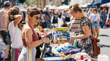 Frau am Grafflmarkt sortiert Stand, andere zeigt Besuchern Produkte, Menschen schlendern vorbei
