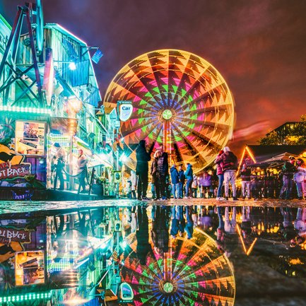Abendstimmung auf der Michaelis-Kirchweih mit leuchtendem Riesenrad, Buden und schlendernden Besuchern