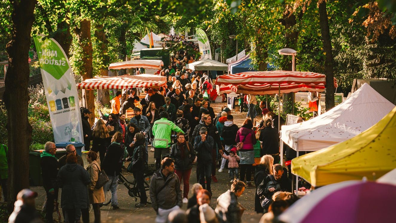 Apfelmarkt mit Marktständen entlang der Stadtpark-Allee, Besucher schlendern unter grünen Bäumen.