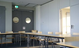 Stuhlreihe im Raum des complex Fürth mit Tür und rundem Fenster im Hintergrund