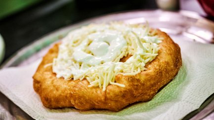 Frisch belegter Langos mit Käse und Sauerrahm auf Serviette und Silberteller am Weihnachtsmarkt.