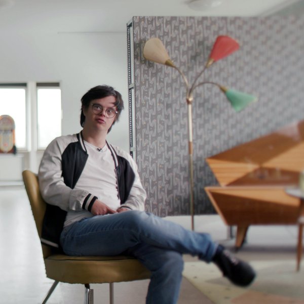 Leo sitzt entspannt auf einem Sessel und führt ein lockeres Gespräch mit dem Dreh-Team.