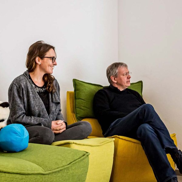 Drei Personen sitzen auf bequemen Sofas und unterhalten sich in einer modernen, entspannten Arbeitsumgebung