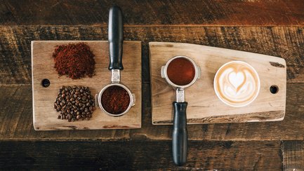 Kaffeebohnen, frisch gemahlenes Pulver und eine fertige Tasse Kaffee.