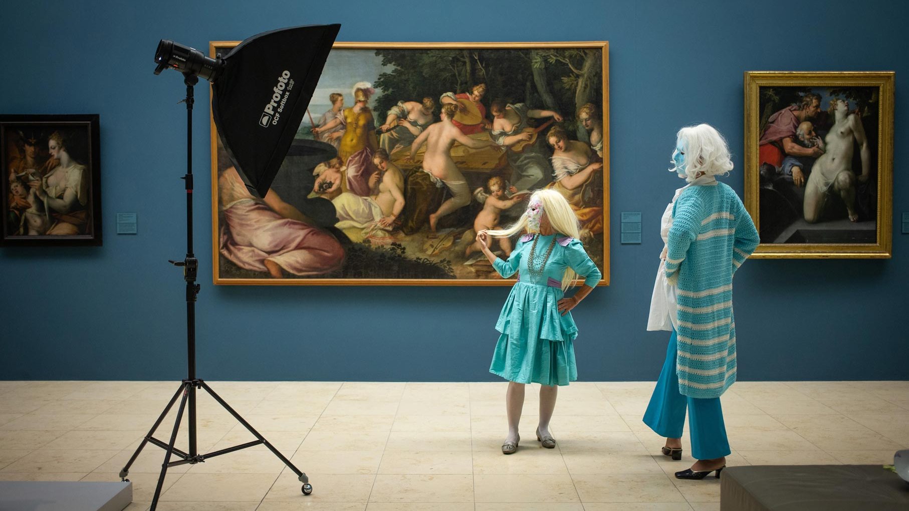 Zwei maskierte Besucherinnen vor historischen Gemälden in einer kunstvollen Galerieumgebung.