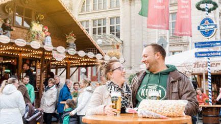 Ein lachendes Paar steht vor einem Ausschankstand auf der Michaelis-Kirchweih und genießt Bier.