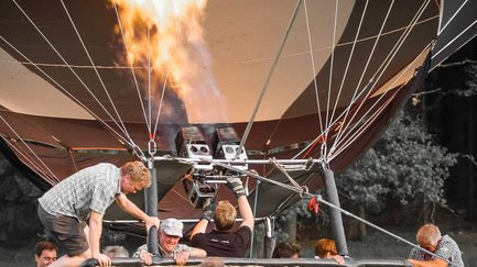 Eine helle Flamme sticht in die Ballonhülle, während Personen für den Start in den Korb einsteigen