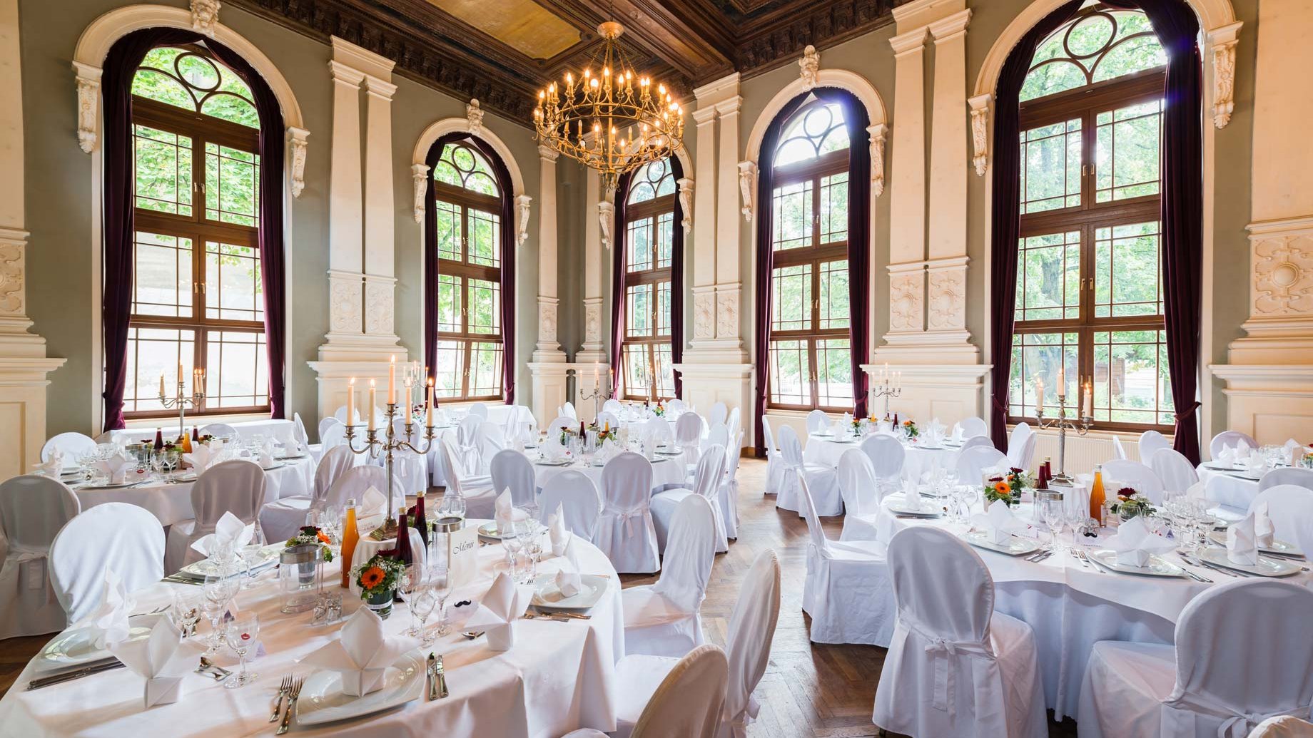 Festlich dekorierter Saal im Logenhaus Fürth mit runden Tischen, Kronleuchter und Blumenarrangements