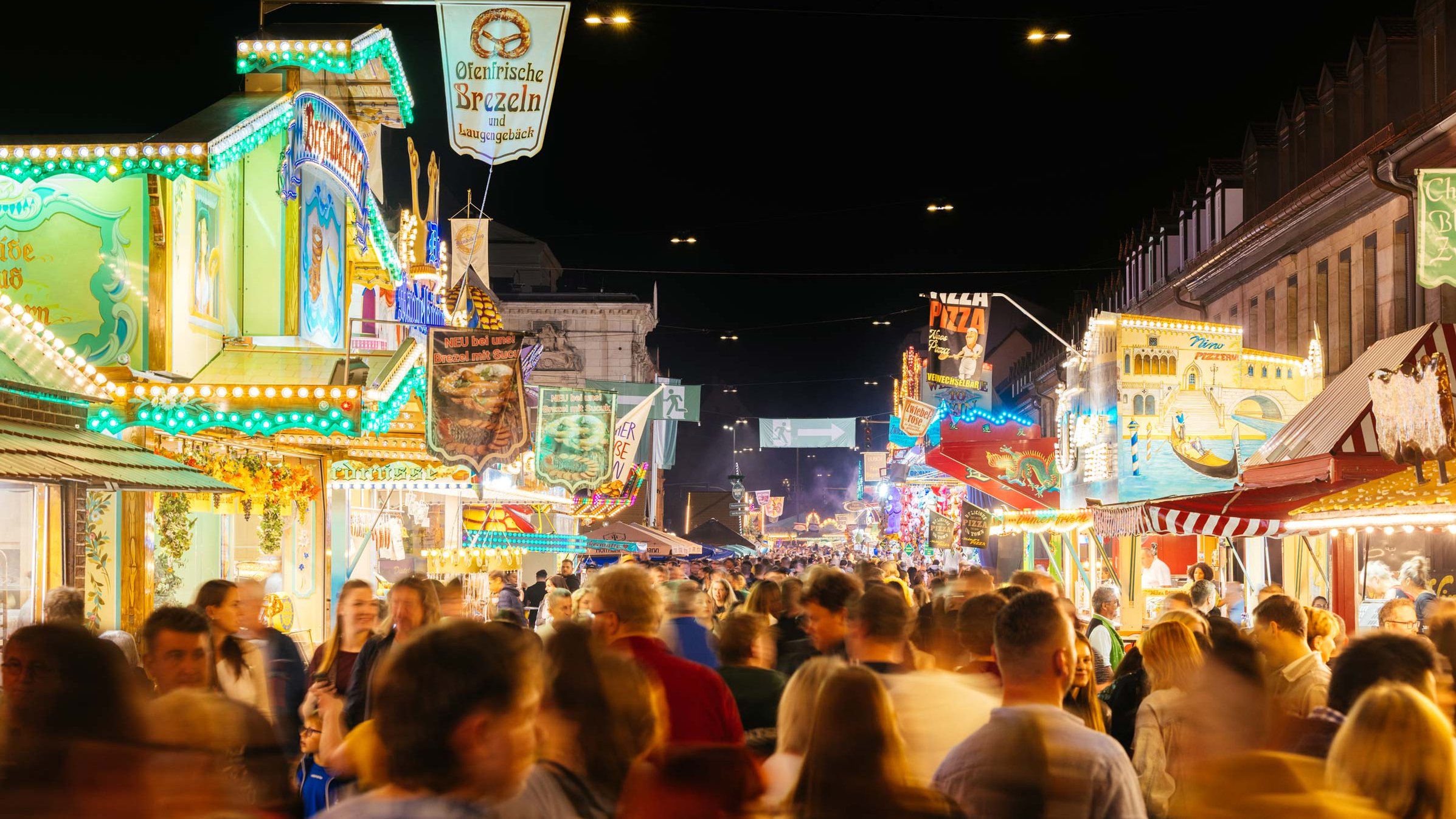 Nächtliche Michaelis-Kirchweih mit Besuchern, die durch bunt beleuchtete Budenstraße schlendern