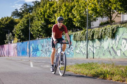 in Radfahrer auf einem Gravelbike fährt an einer langen, bunt bemalten Graffiti-Wand am Europakanal entlang.