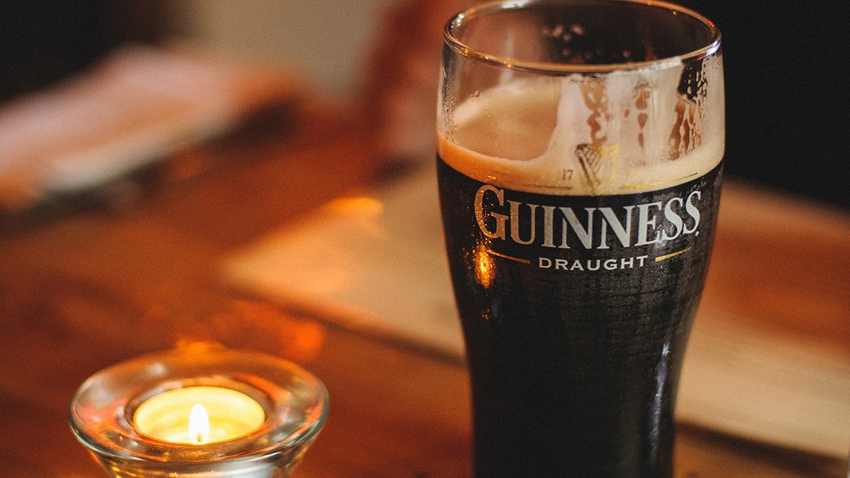 In einem Irish Pub stehen Guinness und ein Teelicht auf einem Holztisch, das eine entspannte Atmosphäre erzeugt.