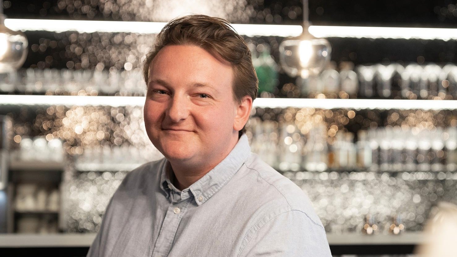 Tim, Chefkoch von Tim’s Kitchen, sitzt an der Theke seines Restaurants, mit Regalen im Hintergrund.