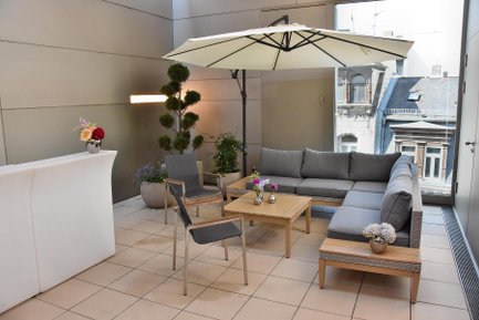 Ecksofa im Veranstaltungsraum mit Schirm und Fensterblick auf historische Sandsteinhäuser