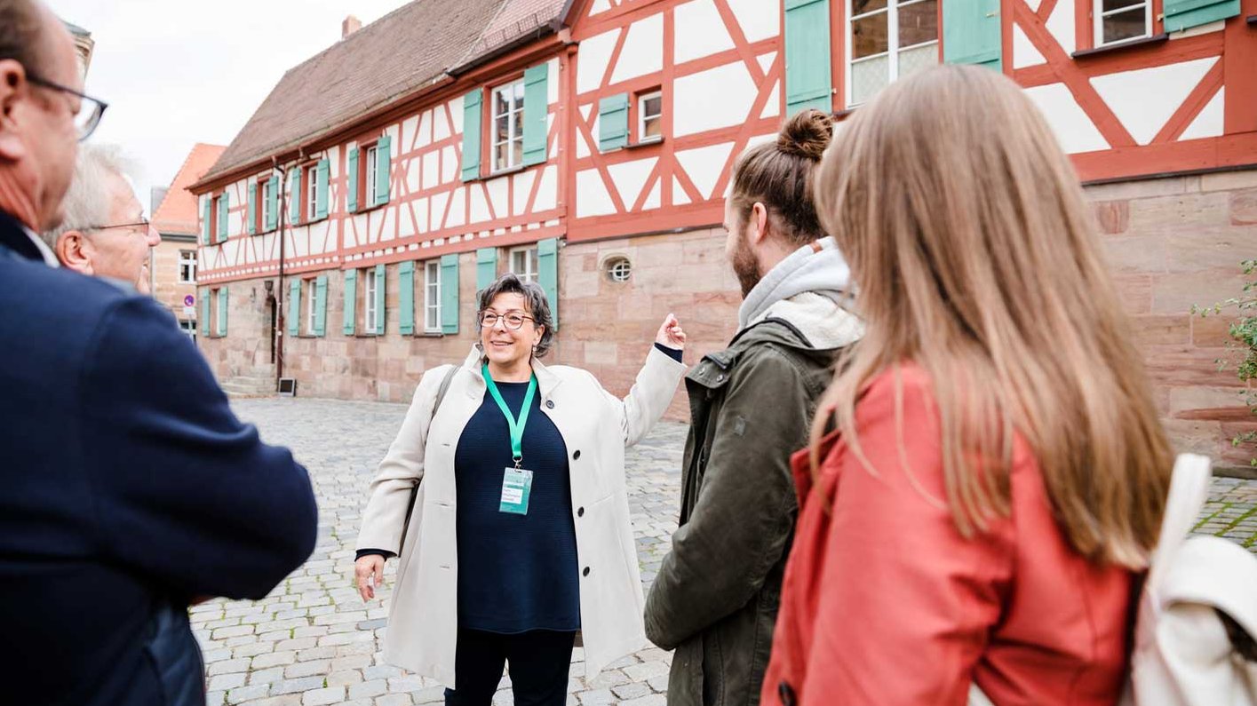 Stadtführerin erklärt einer kleinen Gruppe ein Fachwerkgebäude in Fürth auf gepflastertem Platz