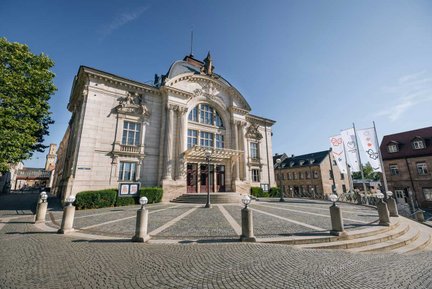 Vorderansicht des Stadttheaters Fürth mit prächtigem Gebäude, Vorplatz und blauem Himmel.