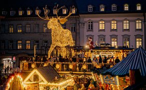 Ein riesiger, leuchtender Elch thront auf einer zweistöckigen Glühweinstube bei Nacht.