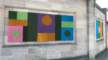 Steinmauer mit farbigen Kunstrasen-Teppichen in geometrischen Mustern.