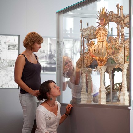 Im Fürther Stadtmuseum betrachten drei Schülerinnen eine Vitrine mit einem alten Kirchweih-Karussell