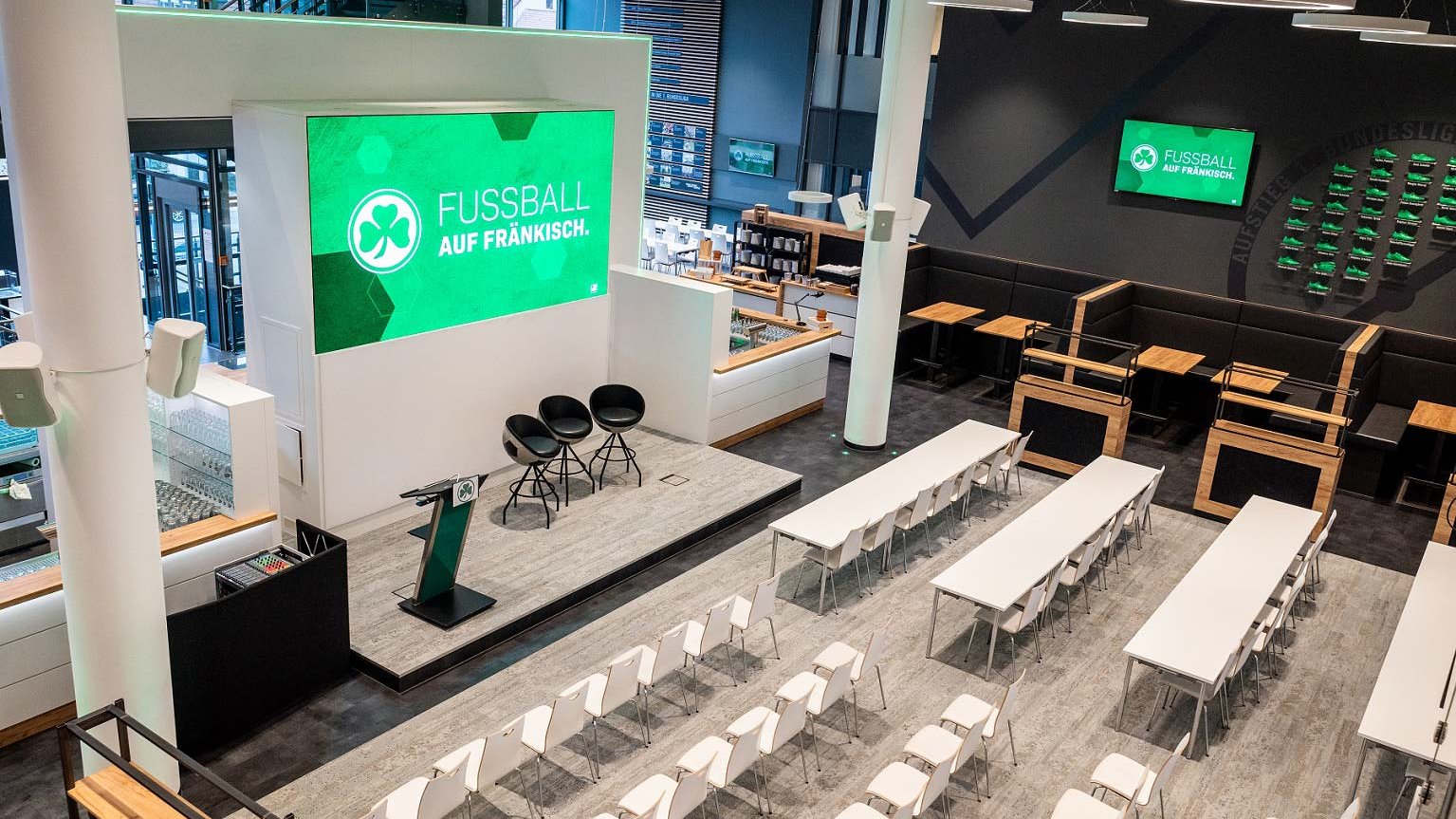 Großzügige, moderne Eventlocation in der Haupttribüne mit Stuhlreihen, Bühne, Rednerpult und Bildschirm