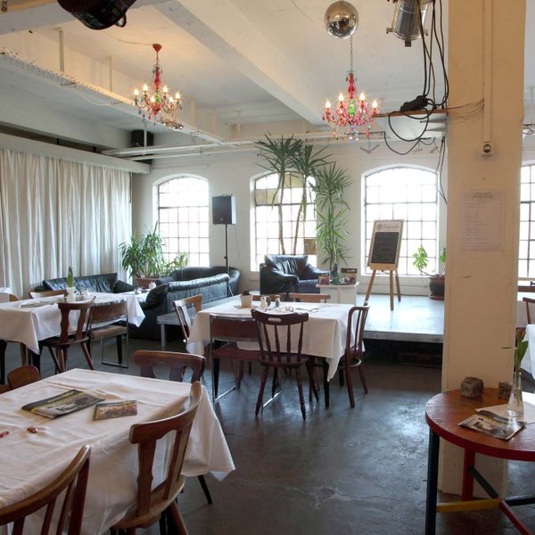 Gemütlicher Raum in der Kofferfabrik Fürth mit Holzstühlen, Bühne, Sofa und großen Industriefenstern