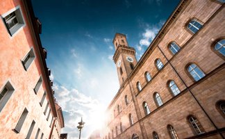 Von unten fotografierter Rathausturm mit Sonne dahinter, blauem Himmel und leichten Wolken.