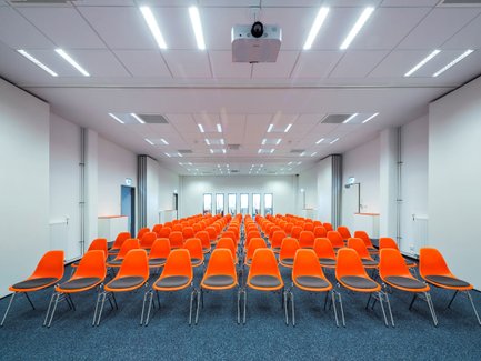Langer Raum bei Neue Materialien Fürth mit Stuhlreihe, orangen Stühlen und Fenster hinten