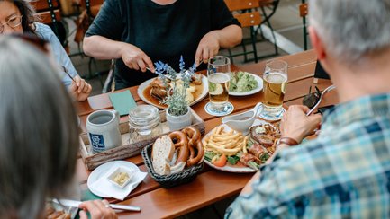 Personen sitzen an einem Holztisch mit fränkischen Gerichten, Brezen und Bier im Biergarten.