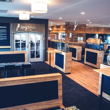 Blick auf modernen Raum der VIP-Tribüne mit Holztischen, Sitzplätzen, Bar und Fußball-Elementen