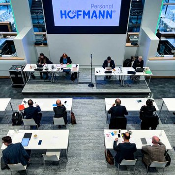Personen auf Bühne und im Publikum bei Veranstaltung von Personal Hofmann, bestuhlt mit Tischen