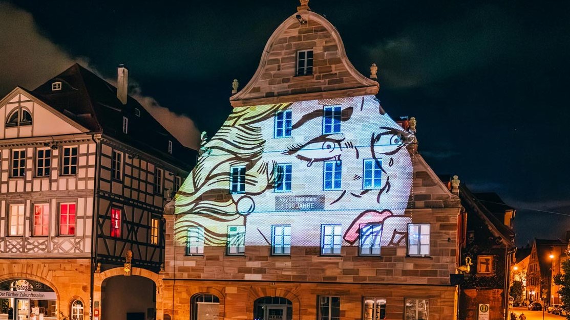 Historisches Haus am Grünen Markt in Fürth bei Glanzlichter, farbig beleuchtet, Besucher bestaunen Lichtkunst.