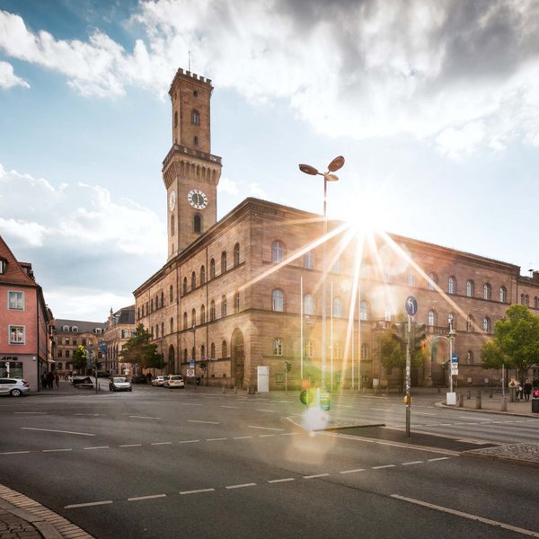 Das Fürther Rathaus mit majestätischem Turm, hinter dem die Sonne hell hervorscheint.