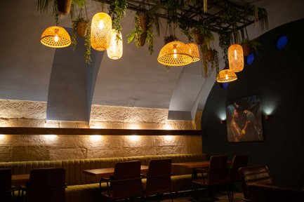 Sitzreihe im Kellergewölbe von Castros Bar mit kunstvollem Bild, warmen Lampen und hängenden Pflanzen