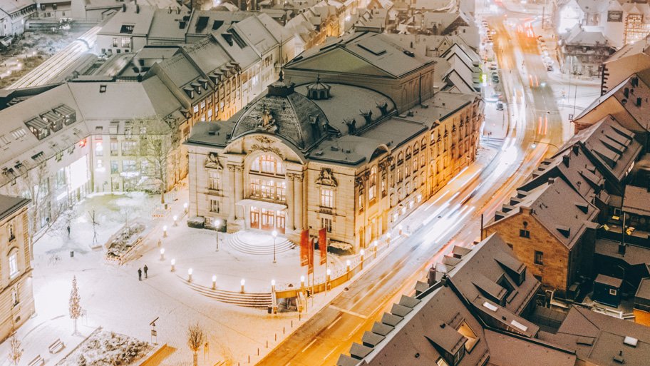 Verschneites Stadttheater aus der Vogelperspektive, dahinter das abendlich beleuchtete Fürther Rathaus