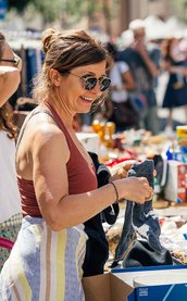 Frau am Grafflmarkt sortiert Stand, andere zeigt Besuchern Produkte, Menschen schlendern vorbei