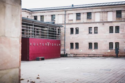 Der gepflasterte Innenhof des Kulturforums Fürth mit roter Fassade und dem Schriftzug der Location.